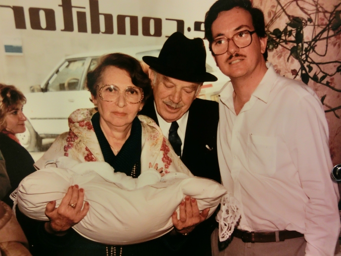 מימין: יגאל אסטרייכר, יחיאל וולץ (חבר המשפחה), אולגה אסטרייכר. בידיה היא מחזיקה את יואב אסטרייכר, שברית המילה שלו התקיימה בבית הקפה באותו יום. 1987